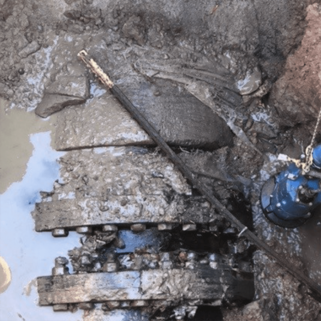 Exposed underground pipe covered in mud and rocks