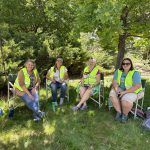 Four women wearing bright yellow vests sitting under the shade of a tree