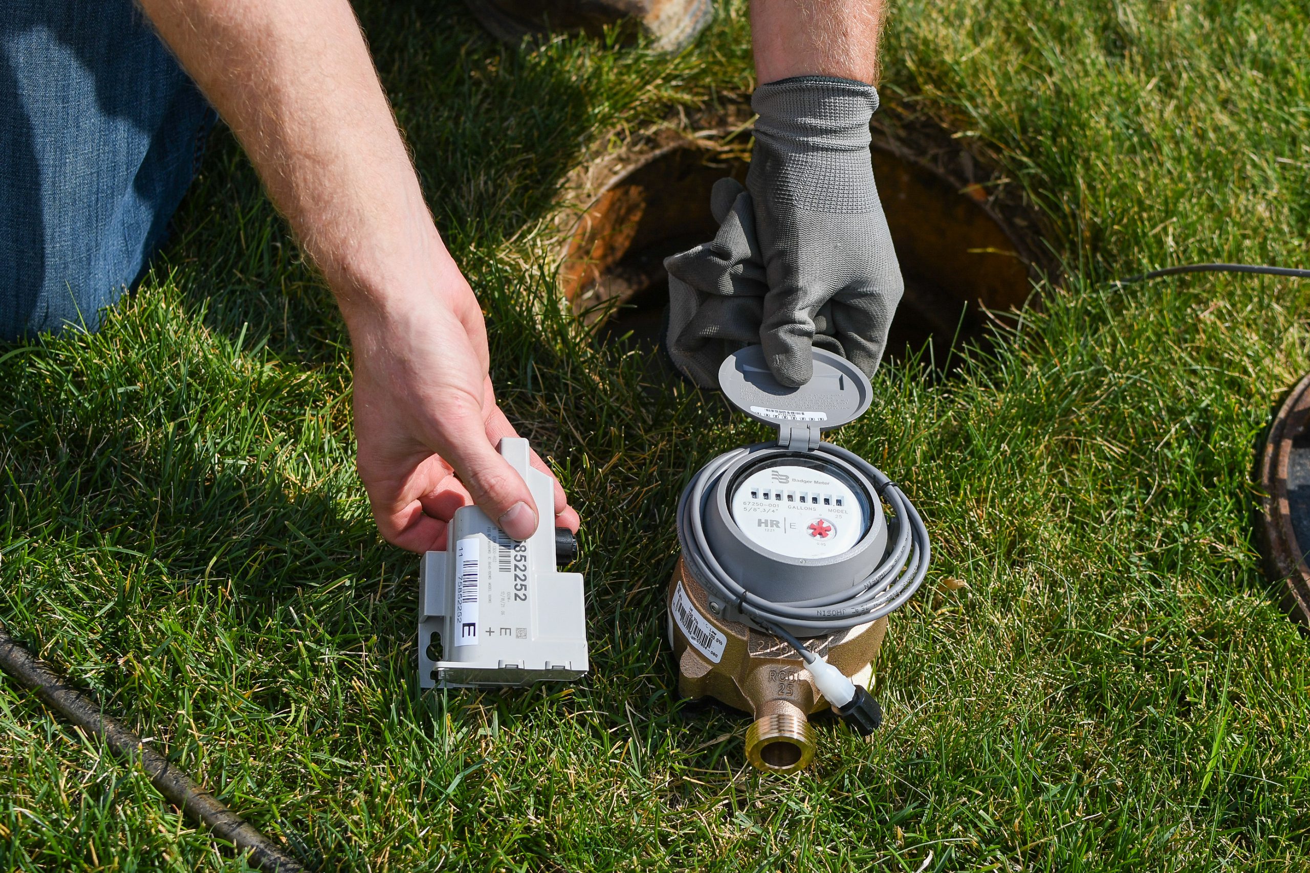 A person knealing on green grass shows updated meter equipment next to an irrigation hole.