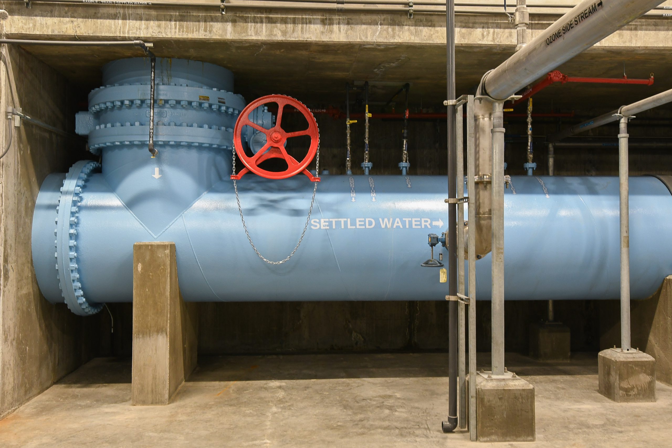 A large blue pipe labeled settled water runs horizontally with a red wheel placed in front to adjust the water flow.