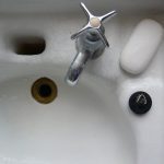 A cracked white sink basin with a turn spout, brass drain pipe and white bar of soap.