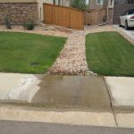 Water on sidewalk draining from the lawn of a residential house with green grass and a rock path