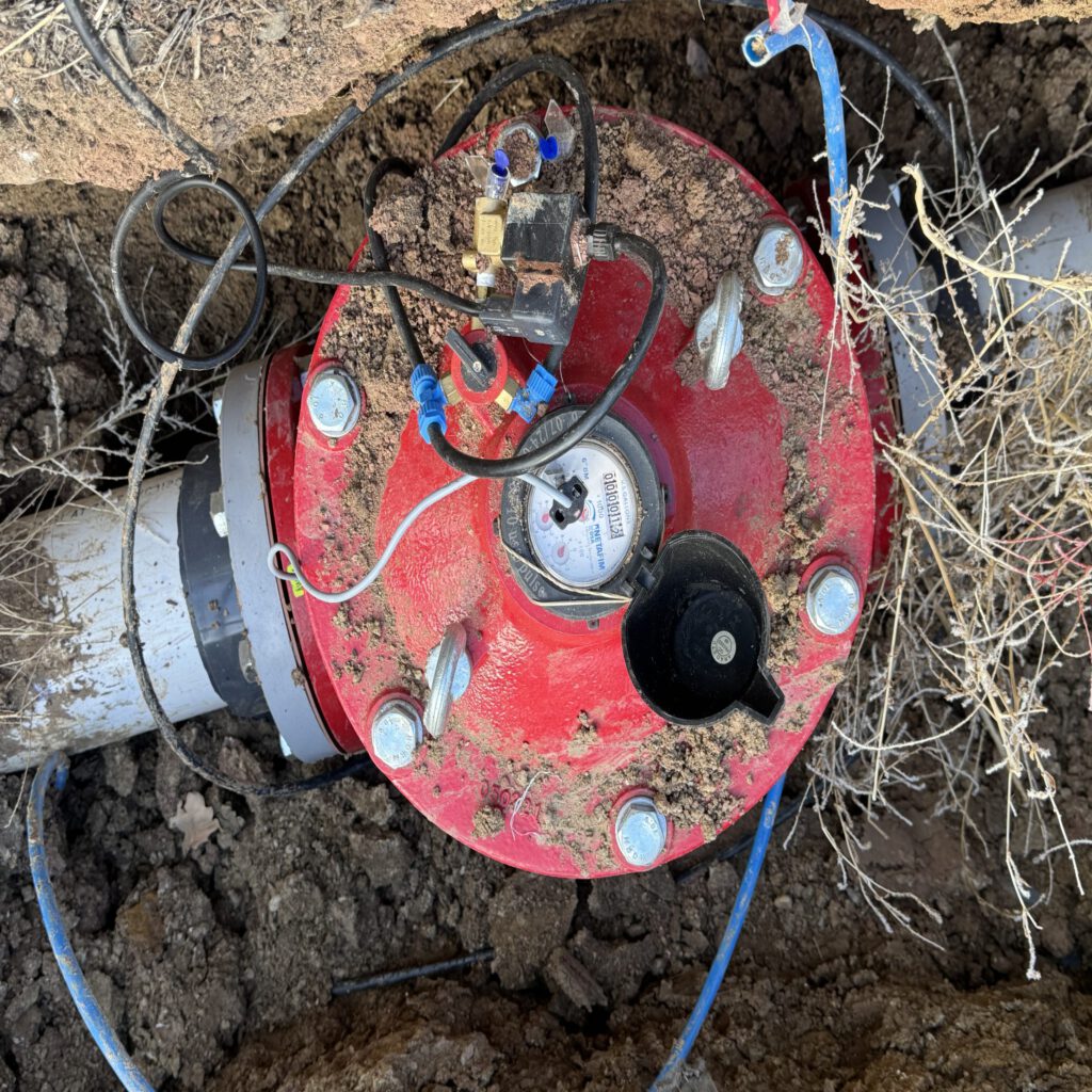Red irrigation system component in the ground with wires and soil surrounding it