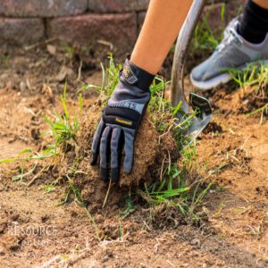 A hand and shovel picking up lawn revealing soil underneath.