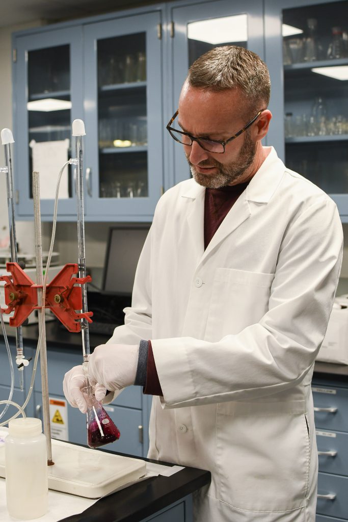 water-treatment-and-quality-031822-5 City of Thornton lab technician wearing a lab coat and completing water titration with a graduated flask and purple liquid.