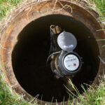 Hole in the grass with a new water meter attached to a pipe.