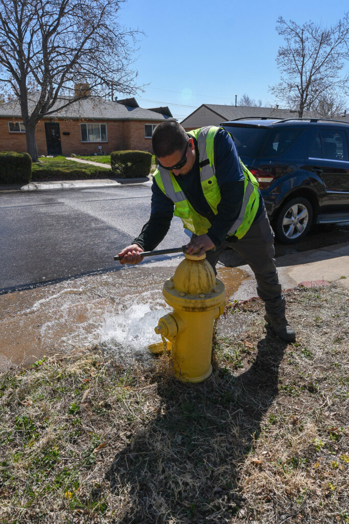 Man in yellow safety vest screws top of yellow fire hydrant gushing water