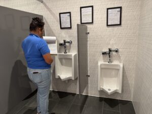 Bree - CII Audit - Urinal Person in a blue shirt holding a clipboard standing in front of a urinal.