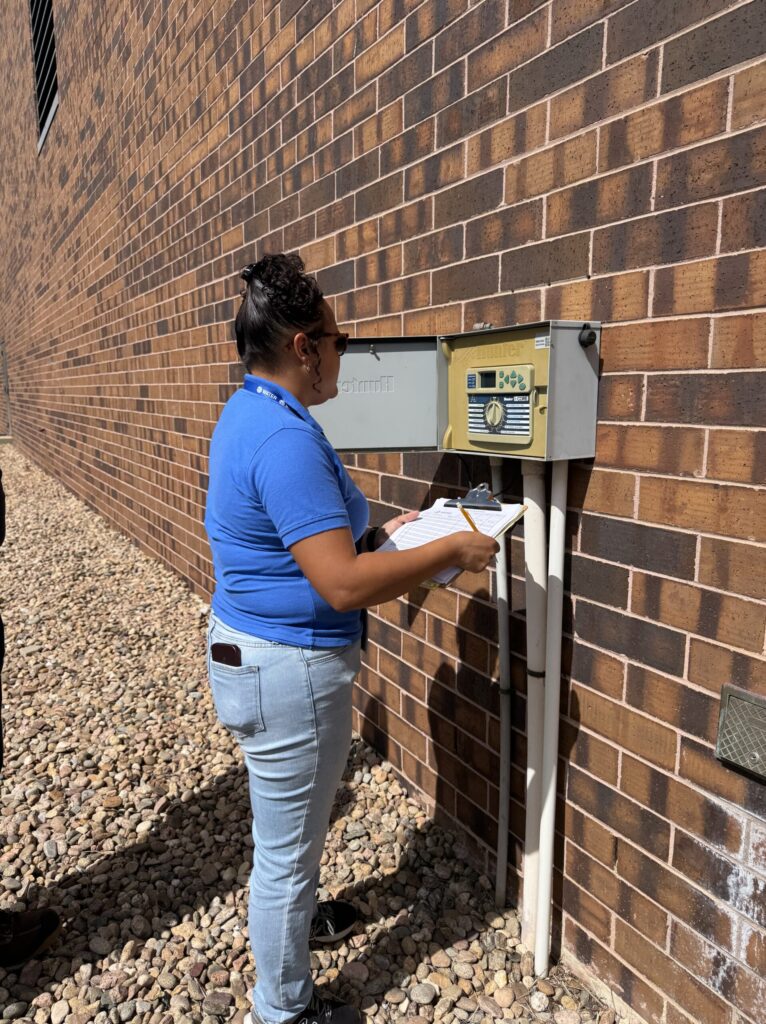 Bree - Irrigation Controller - CII Audit Person in blue shirt holding a clipboard and standing in front of an open irrigation controller panel.
