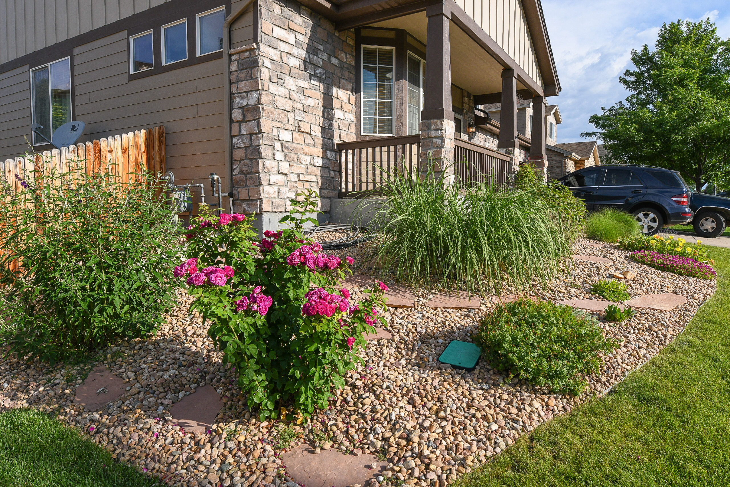 front-yard-water-wise-area A house with rocks and flagstone near the front porch and fence of the house. Roses, a Butterfly bush, ornamental grasses and other water-wise plants are throughout the landscape.